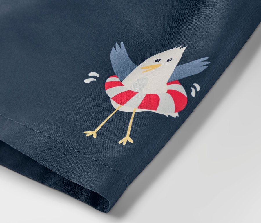 Zbliżenie na dziecięce szorty plażowe we wzór morski, z nadrukiem mewy w kole ratunkowym.