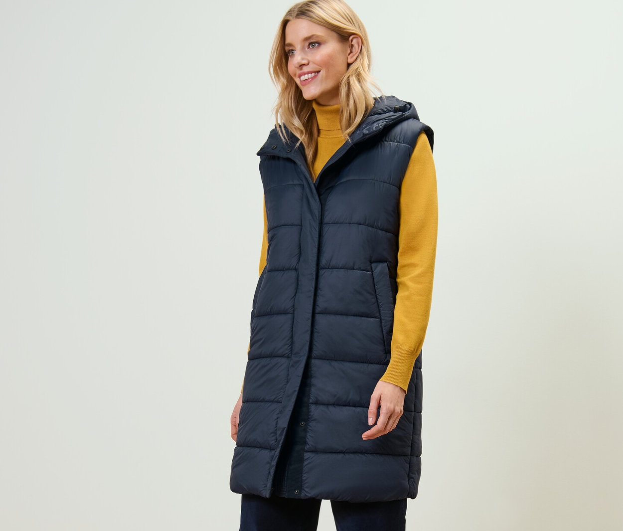 Kobieta ma na sobie długą pikowaną kamizelkę z kapturem.