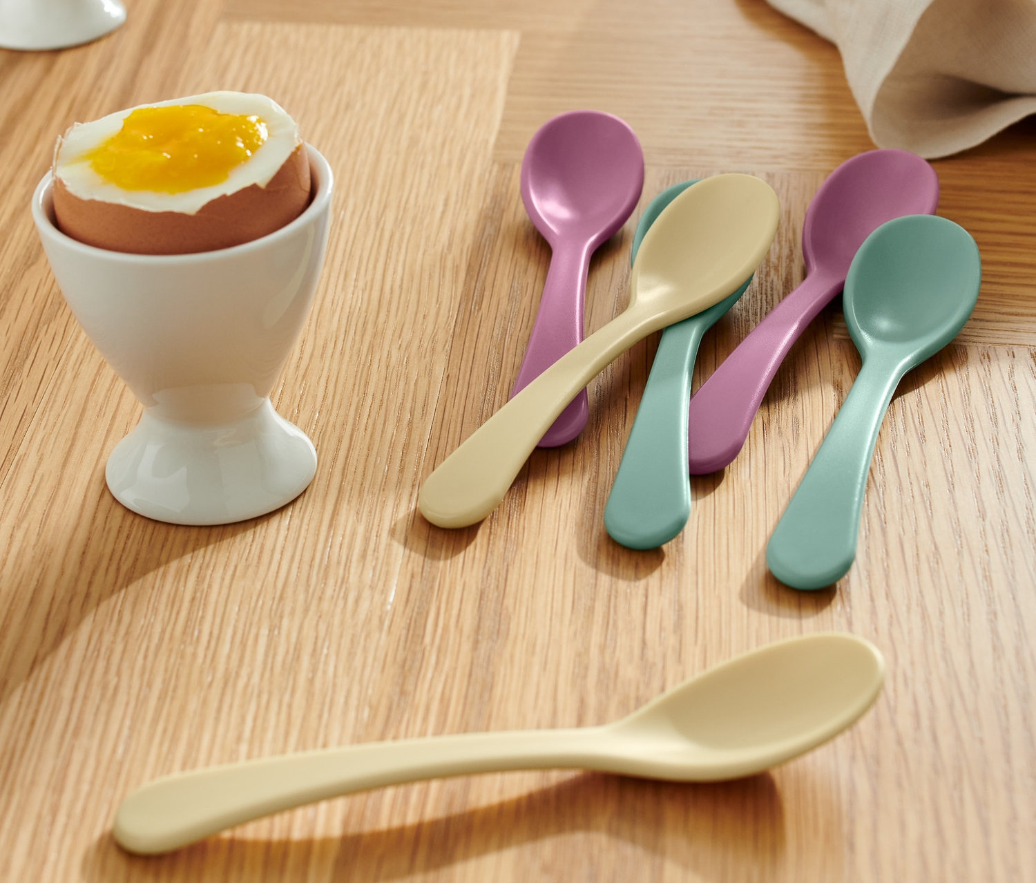 Na drewnianym stole widoczne są jajka w białych kieliszkach i Łyżeczki do jajek, 6 sztuk.