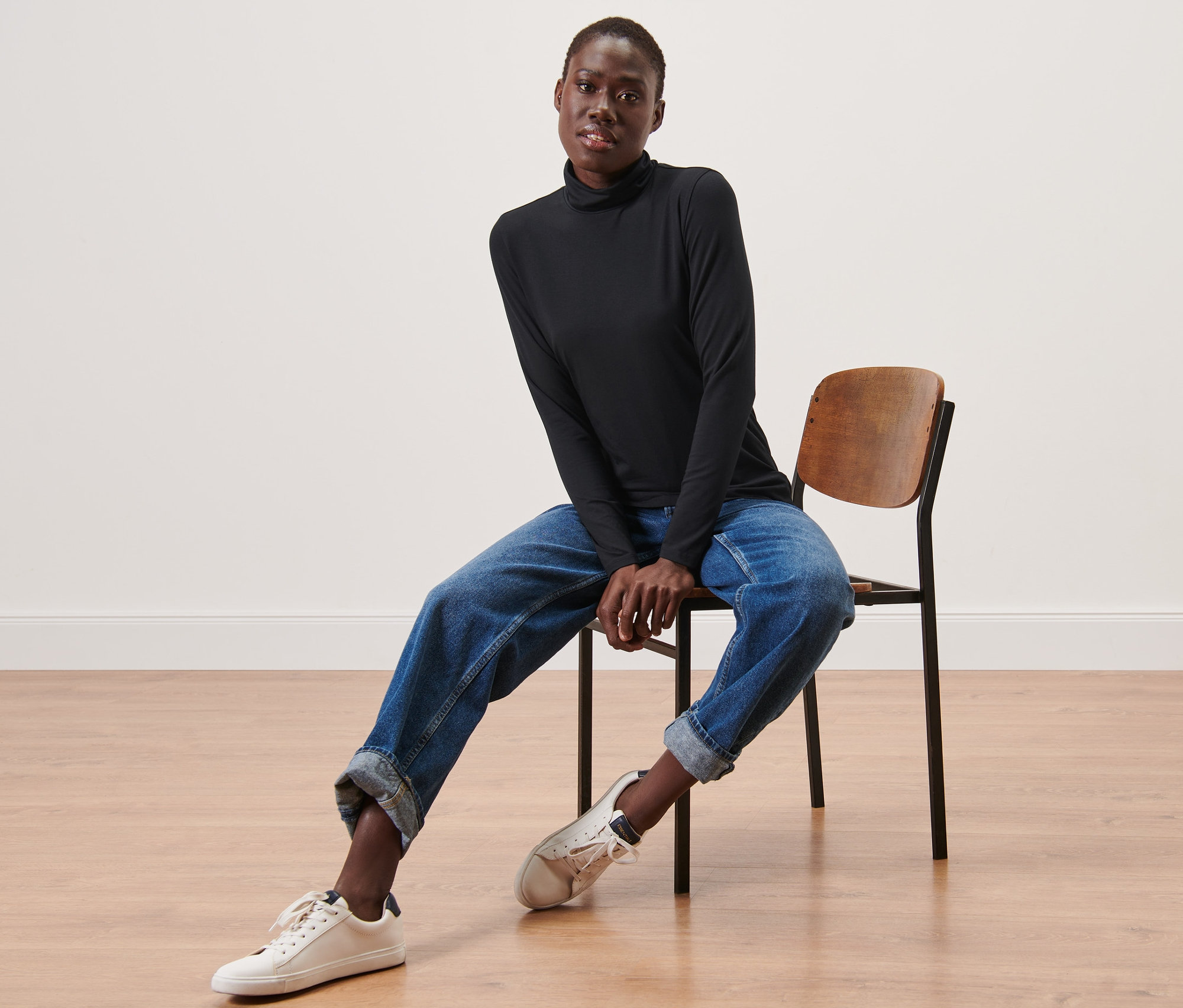 Kobieta siedzi na krześle i ma na sobie czarną koszulkę z golfem.