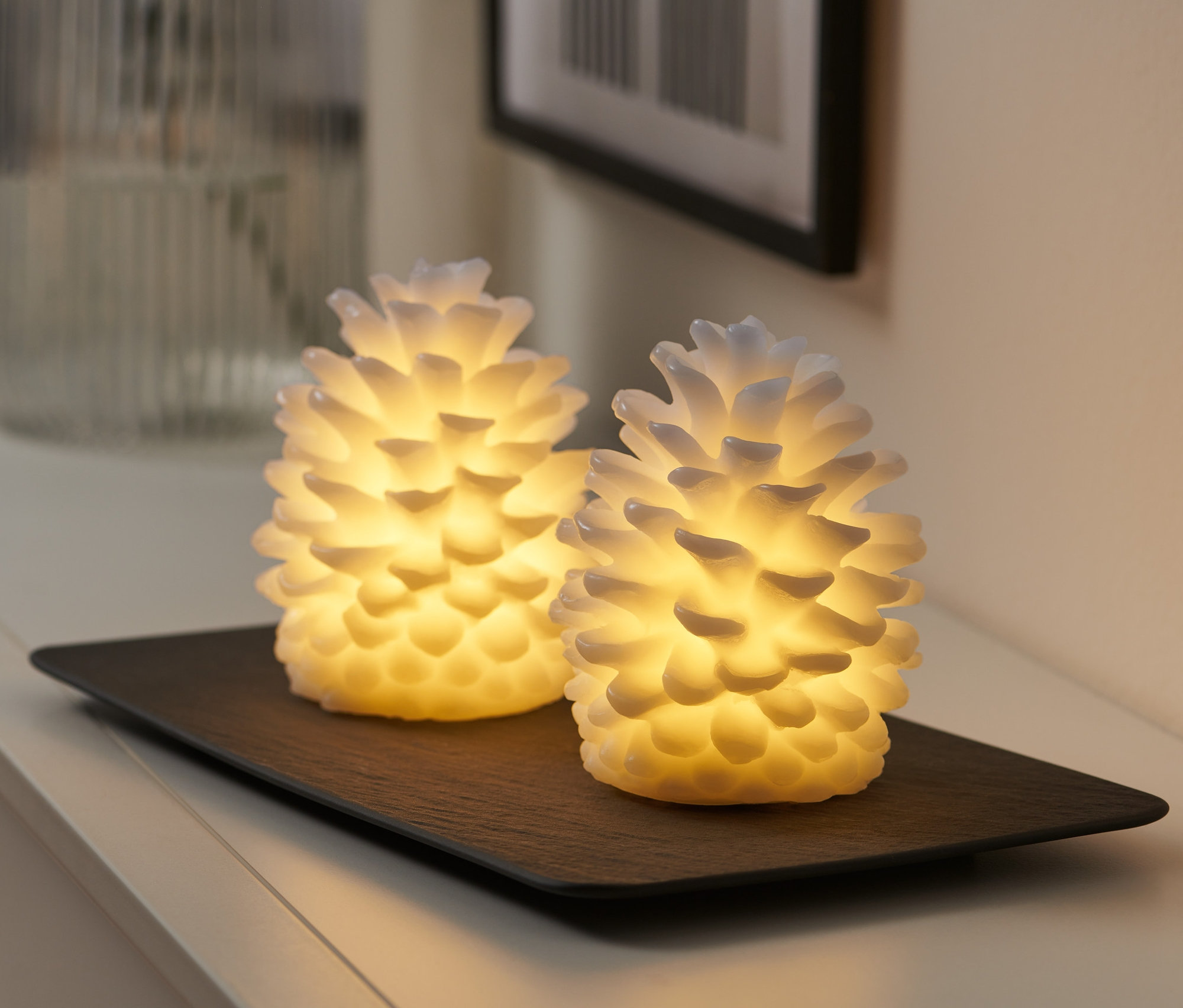 Dwie szyszki LED z prawdziwego wosku na czarnej tacy.