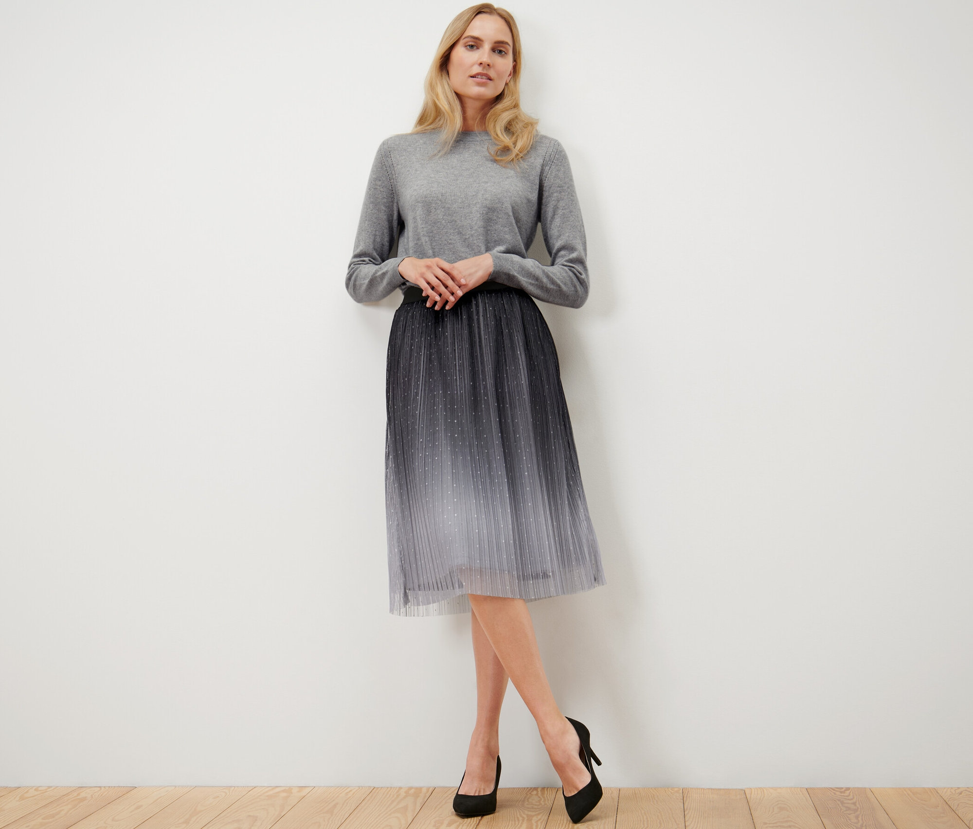 Kobieta pozuje, ubrana w plisowaną spódnicę z tiulu z gradientem.