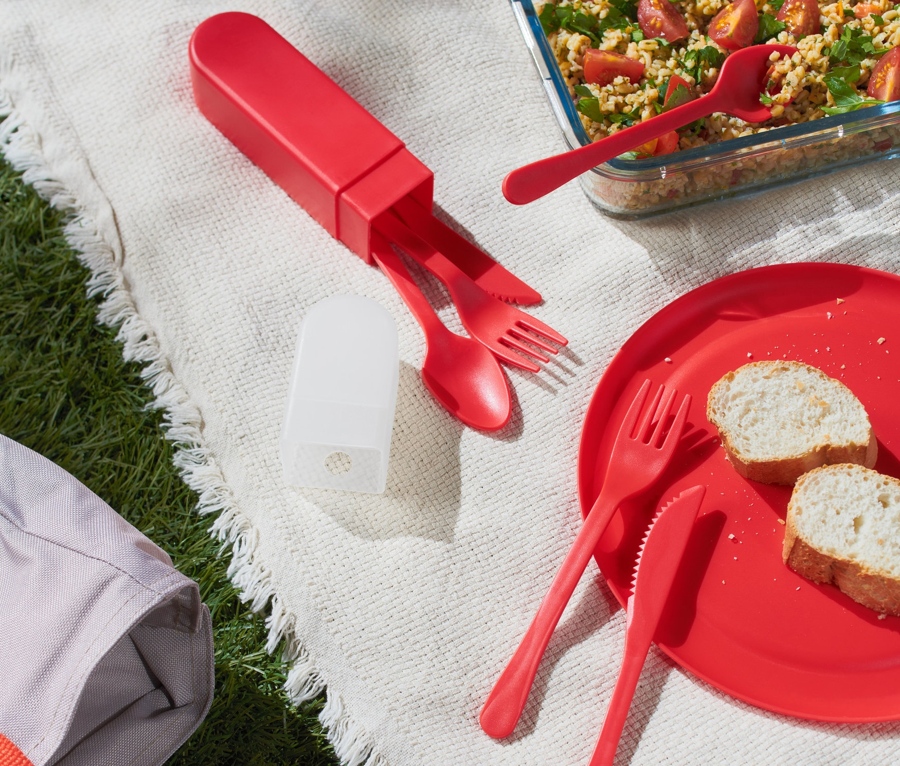 Czerwone sztućce piknikowe na kocu z jedzeniem.