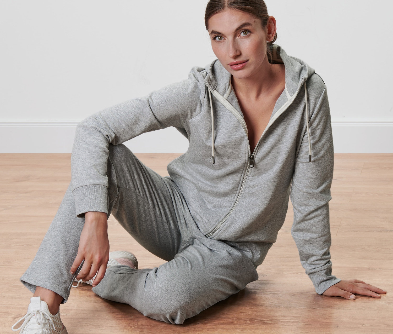 Kobieta siedzi na podłodze w szarej bluzie z dzianiny dresowej.