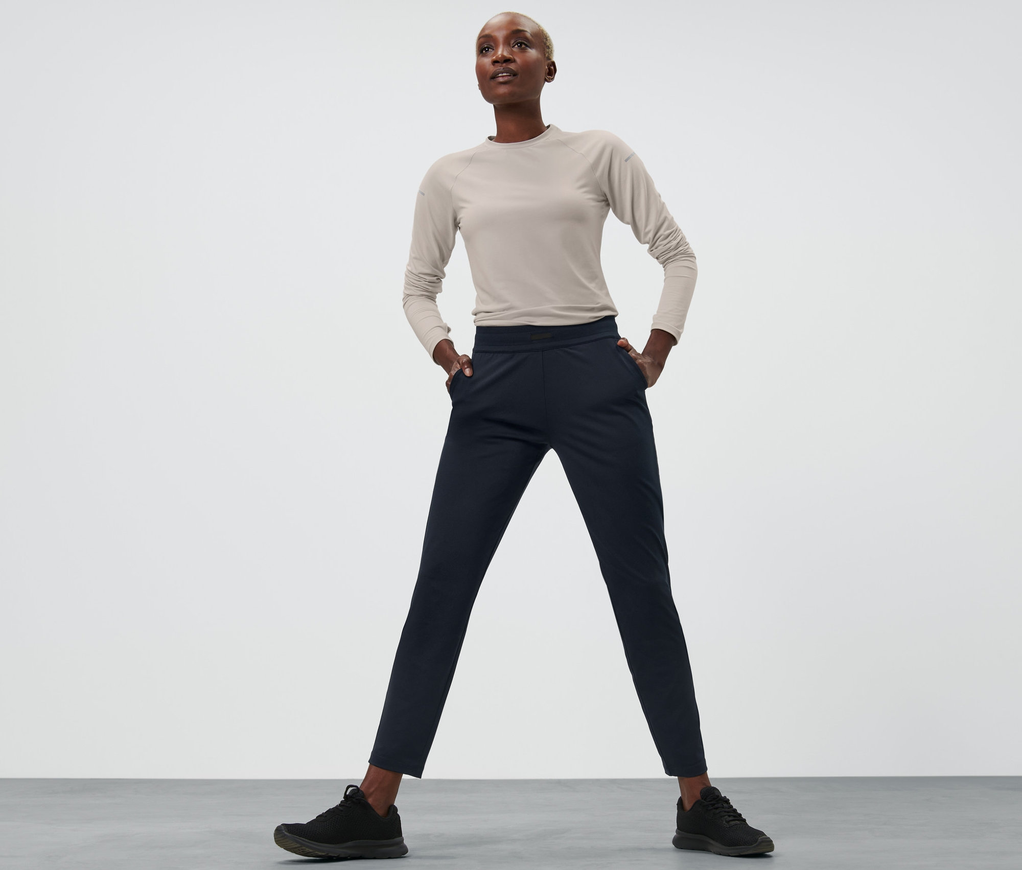 Kobieta stoi z rękami w kieszeniach spodni treningowych.