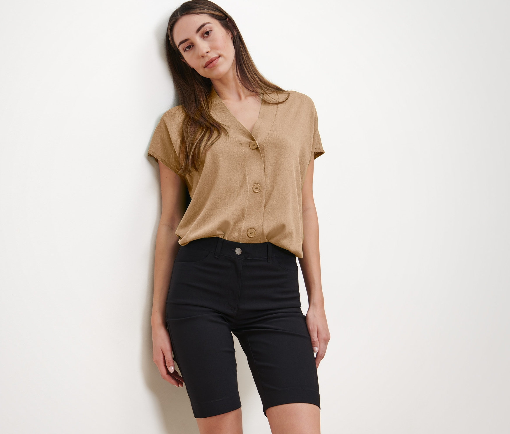 Kobieta pozuje w beżowej bluzce i czarnych szortach bermudach z bengaliny.