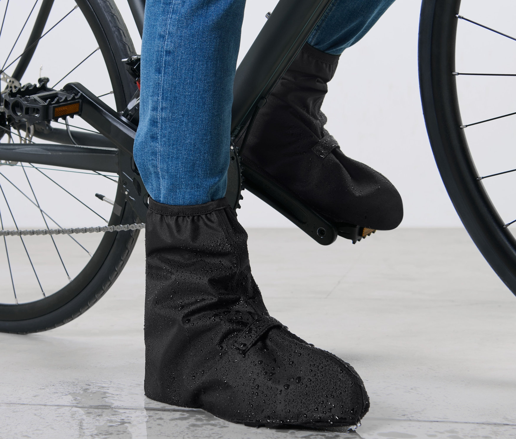 Stopy rowerzysty w niebieskich dżinsach i czarnych przeciwdeszczowych ochraniaczach na buty na rowerze.