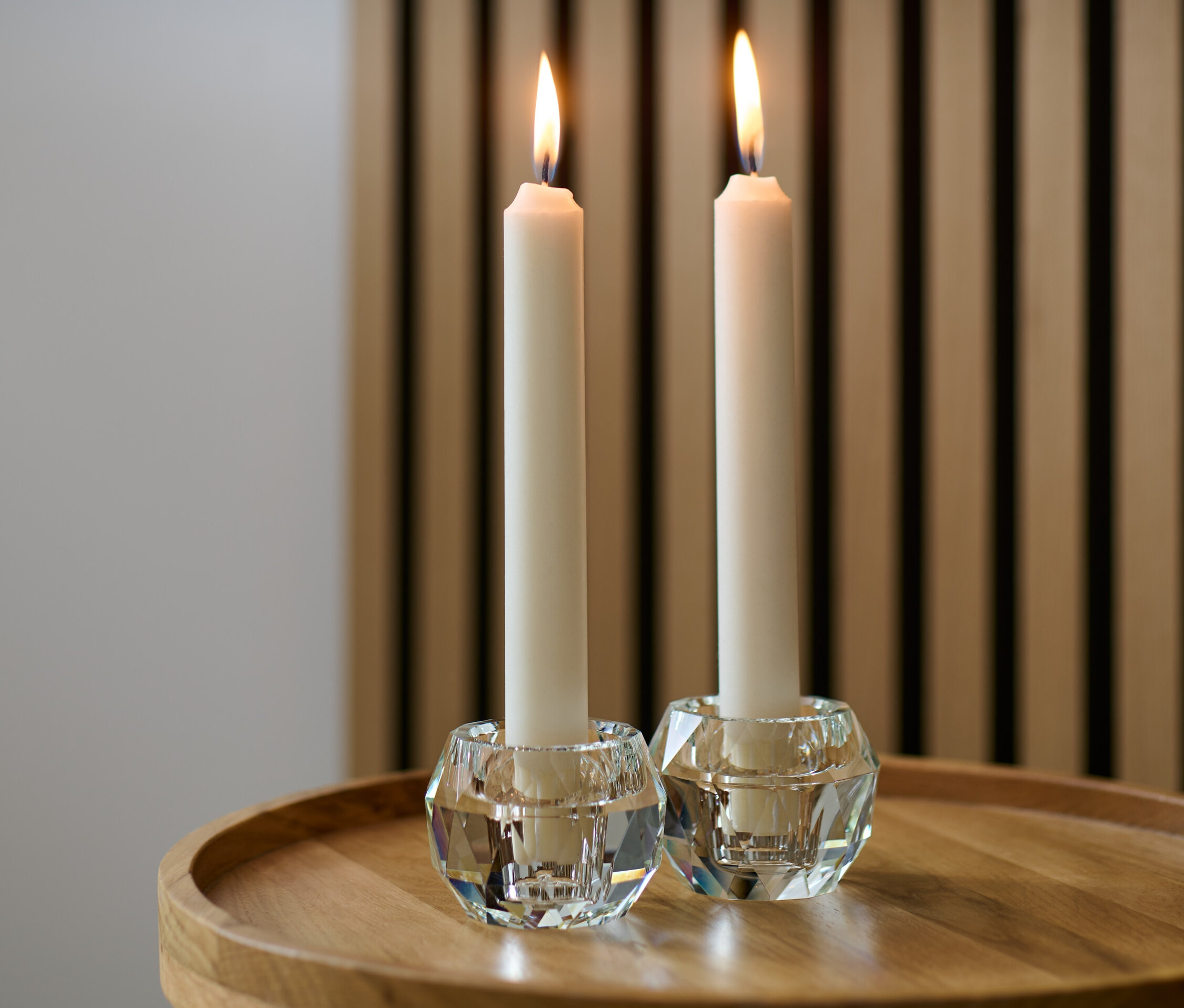 Dwa szklane świeczniki z płonącymi świecami na drewnianym stole.