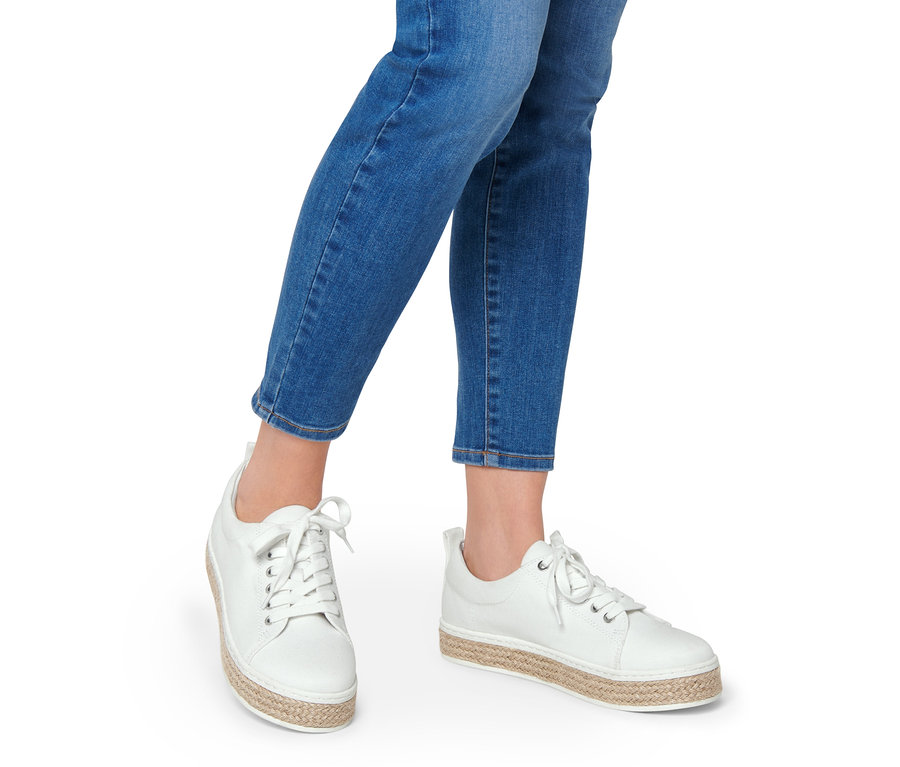 Nogi kobiety w dżinsach i białych płóciennych sneakersach.