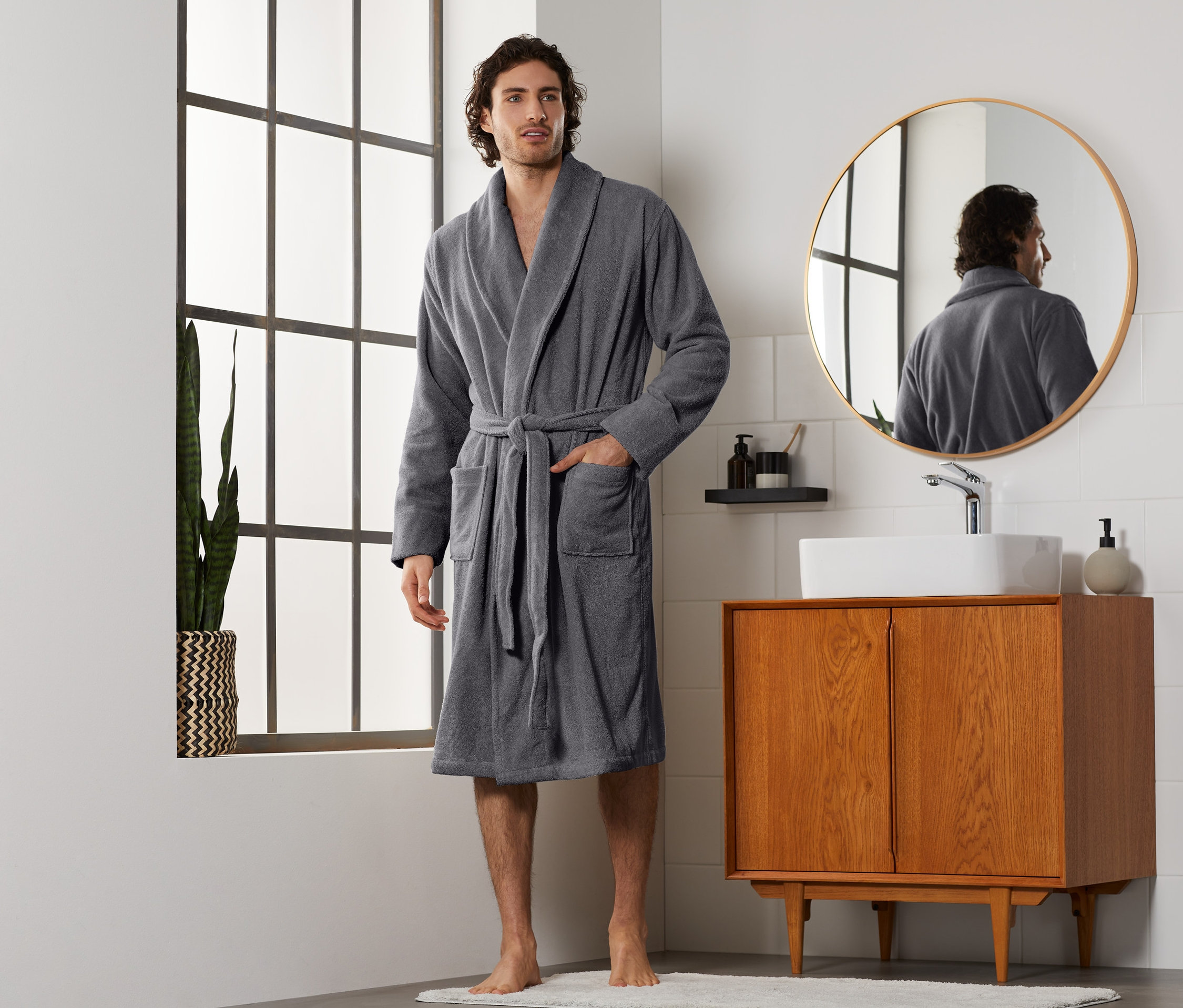 Mężczyzna w szarym szlafroku męskim stoi w łazience.