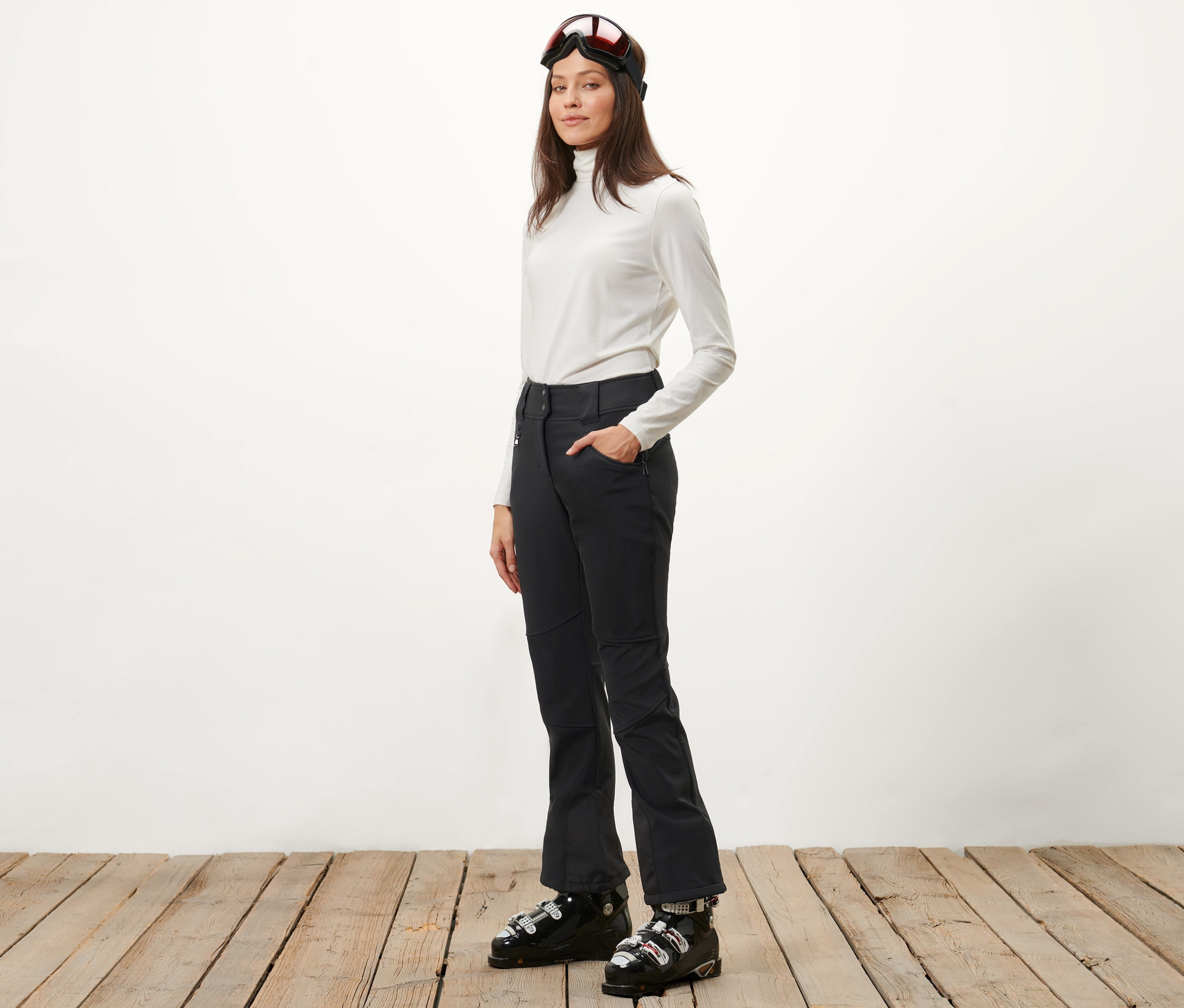 Kobieta pozuje w spodniach narciarskich i butach narciarskich.