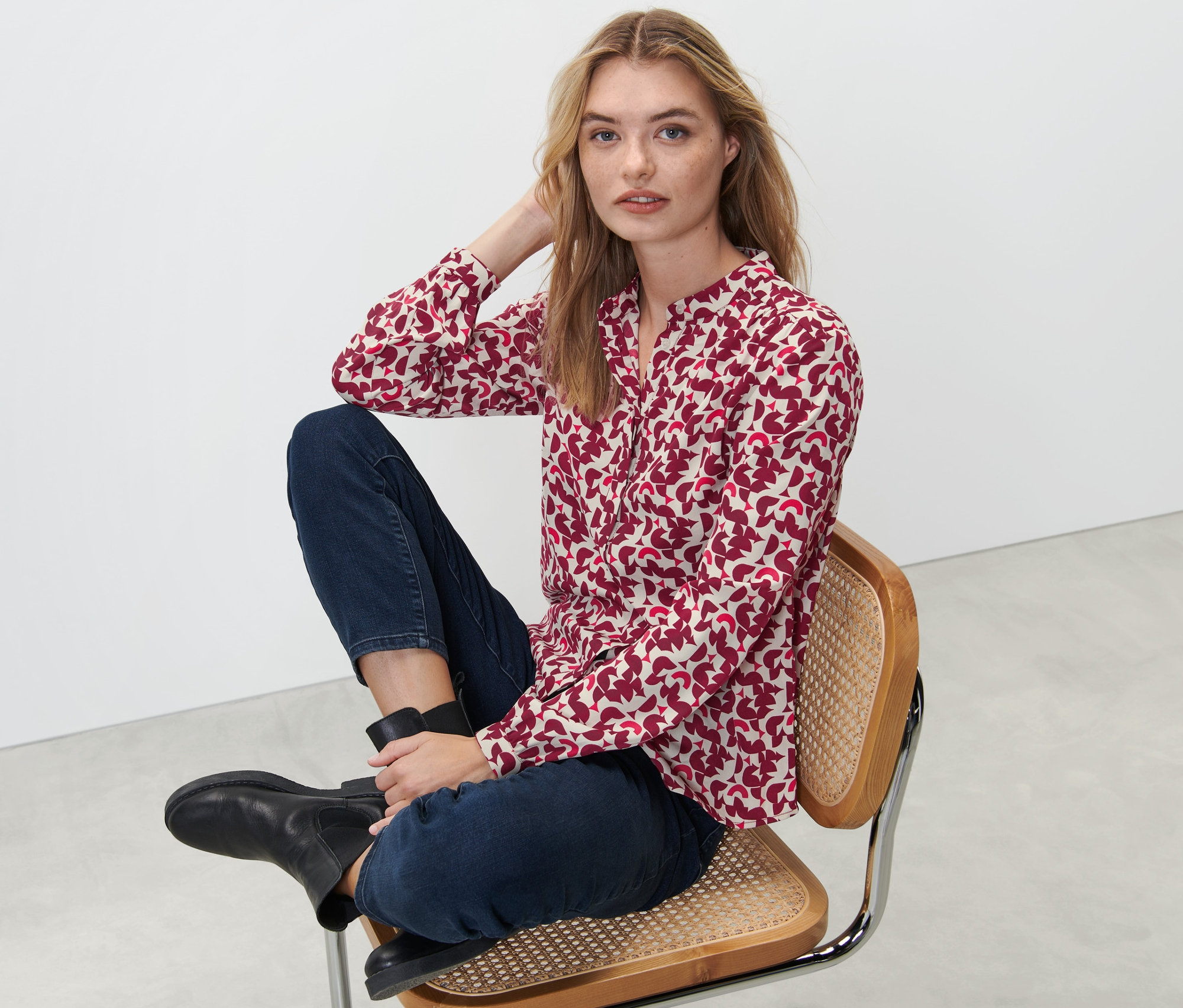 Kobieta siedzi na krześle i ma na sobie bluzkę z nadrukiem.