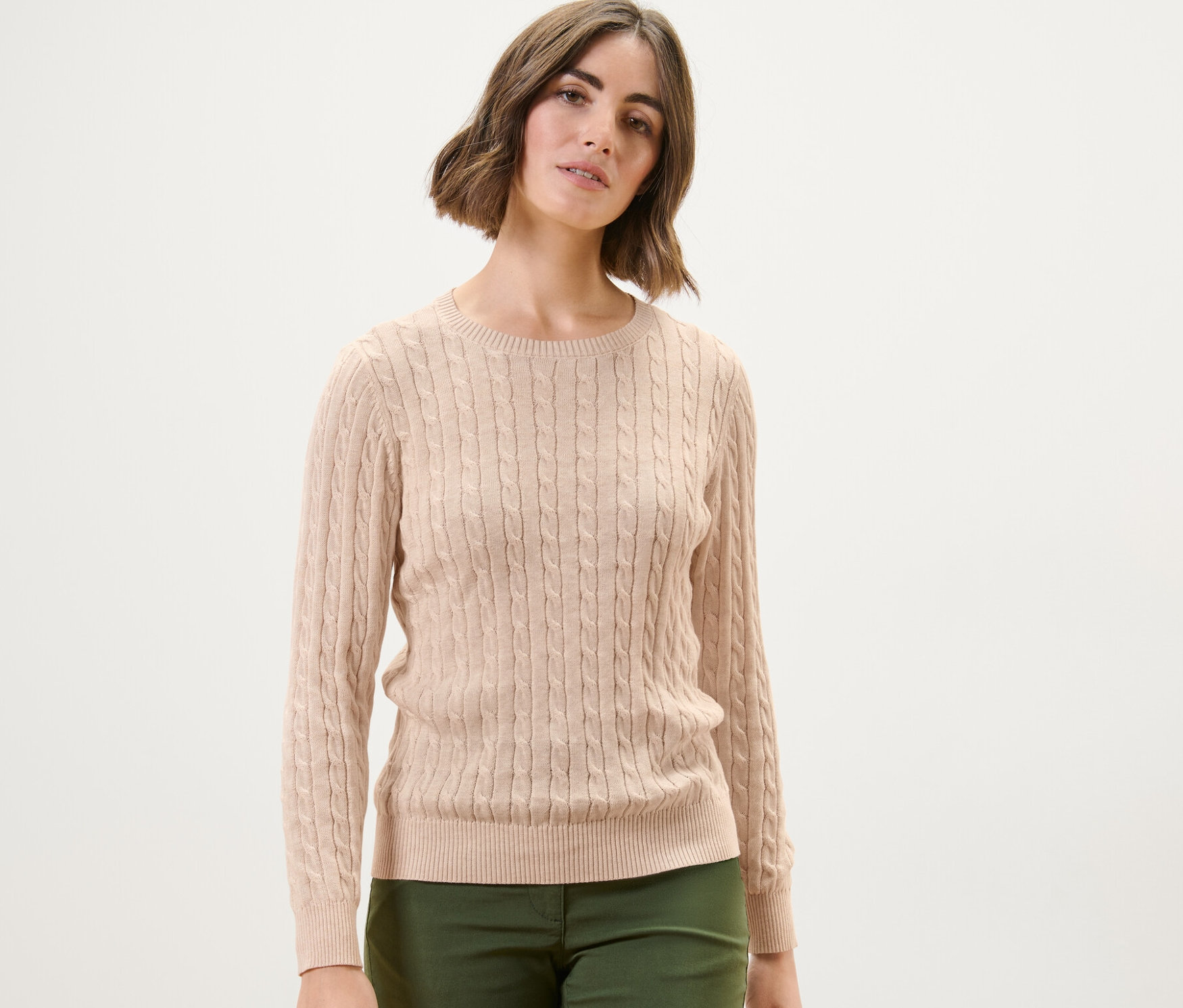 Kobieta ma na sobie kremowy sweter z warkoczowym wzorem.