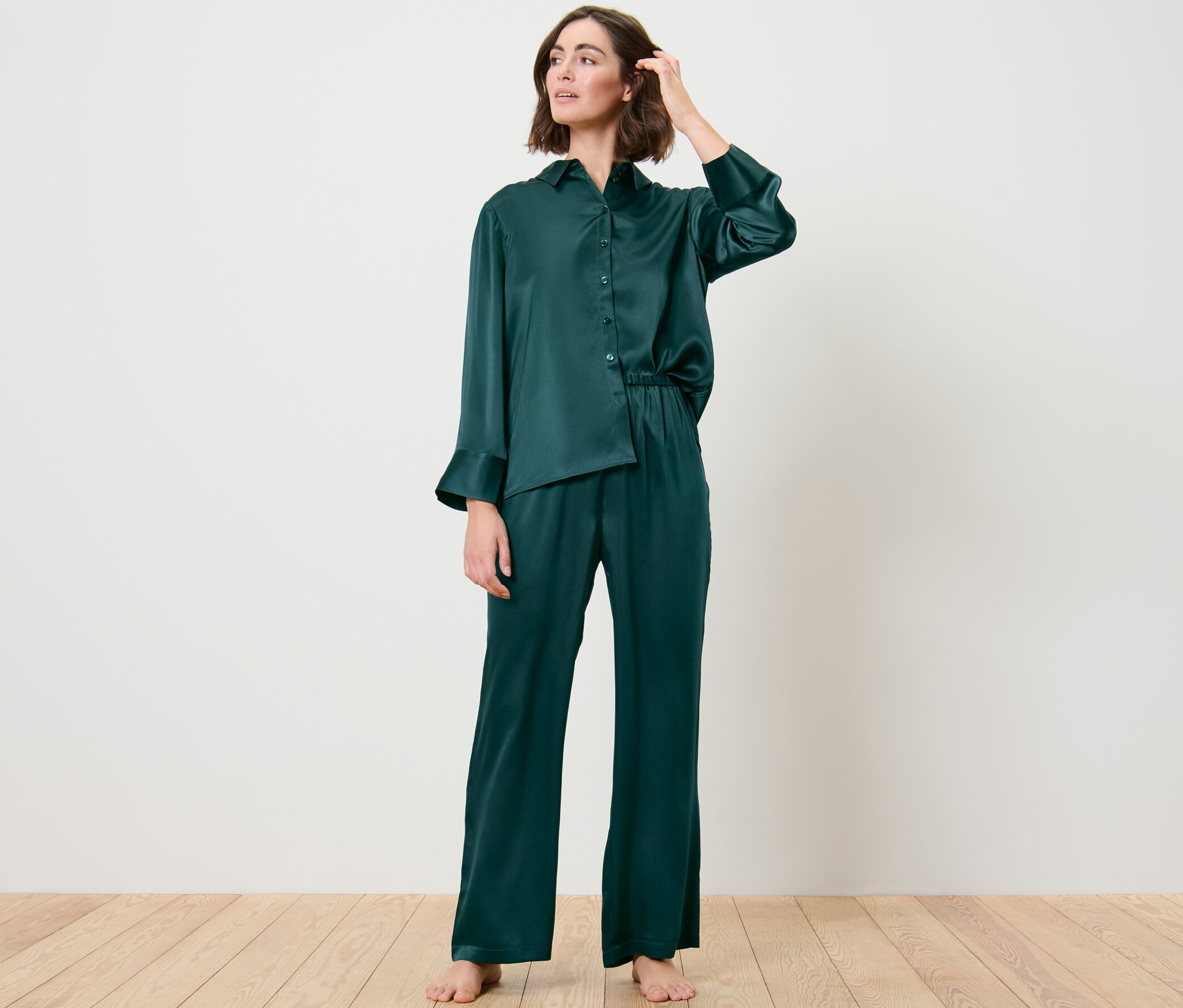 Kobieta ma na sobie jedwabne spodnie od piżamy i pozuje w pokoju.