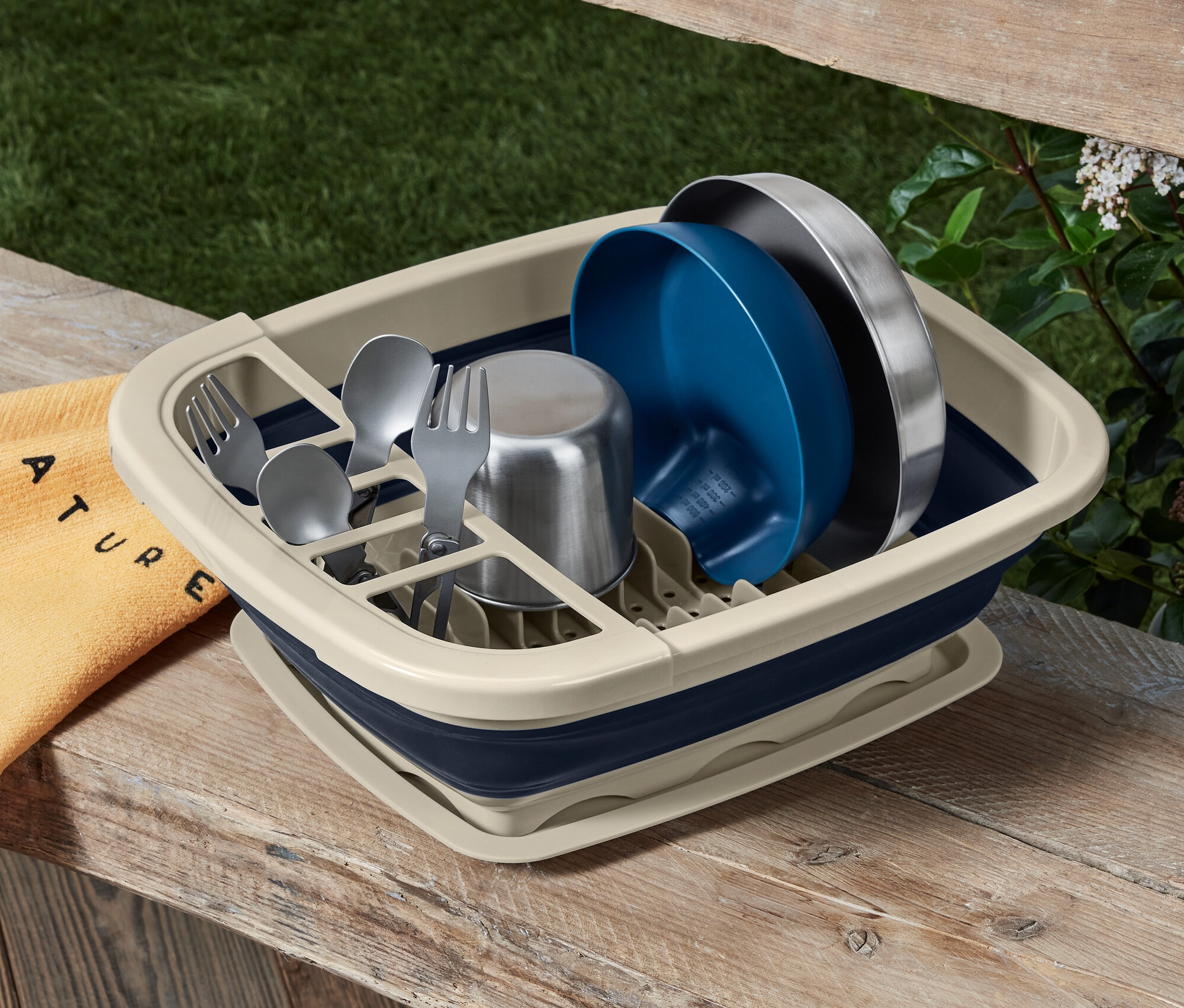 Składana suszarka do naczyń z naczyniami i sztućcami na drewnianym stole.