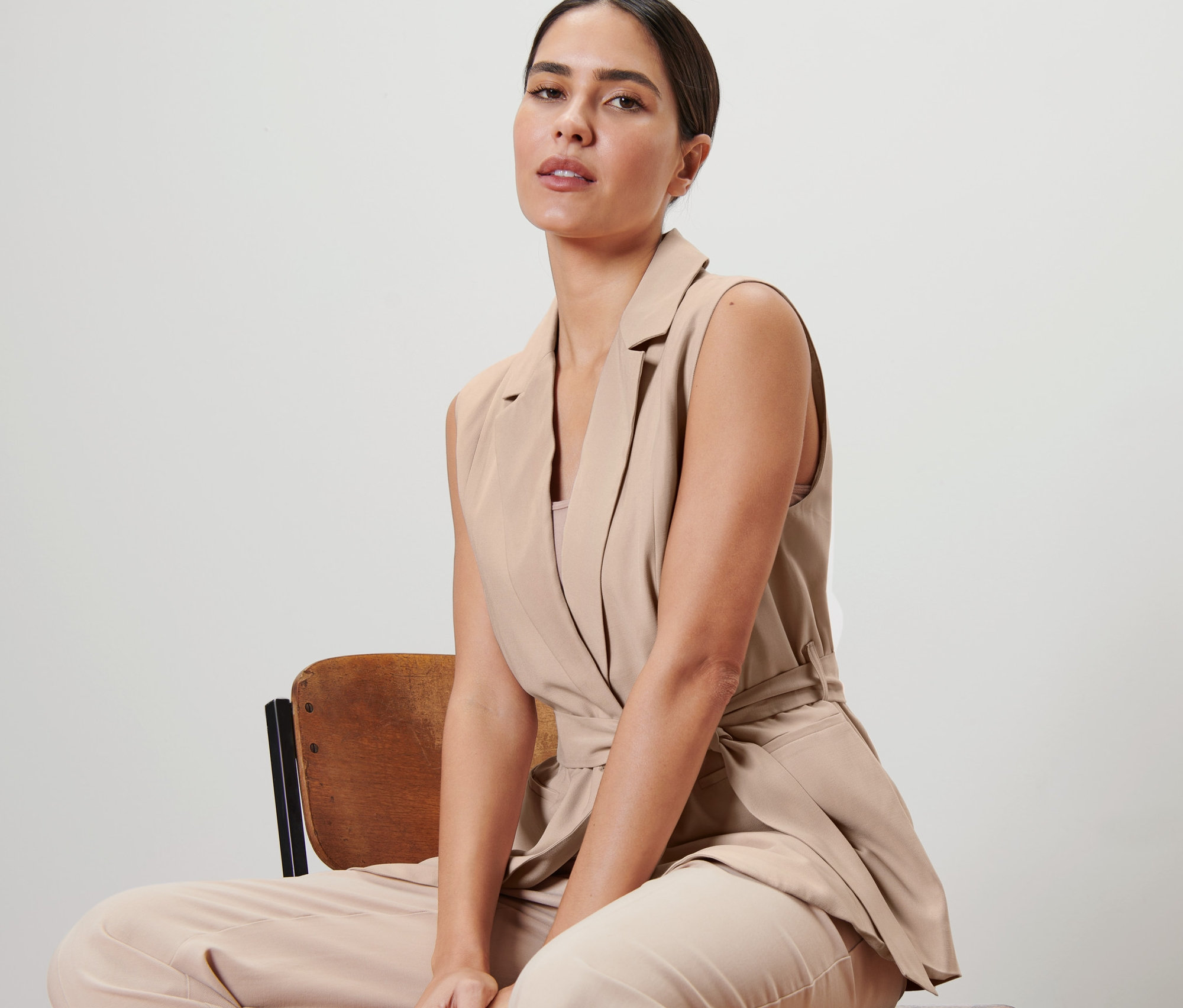 Kobieta siedzi na krześle i ma na sobie kamizelkę z wiązanym paskiem.