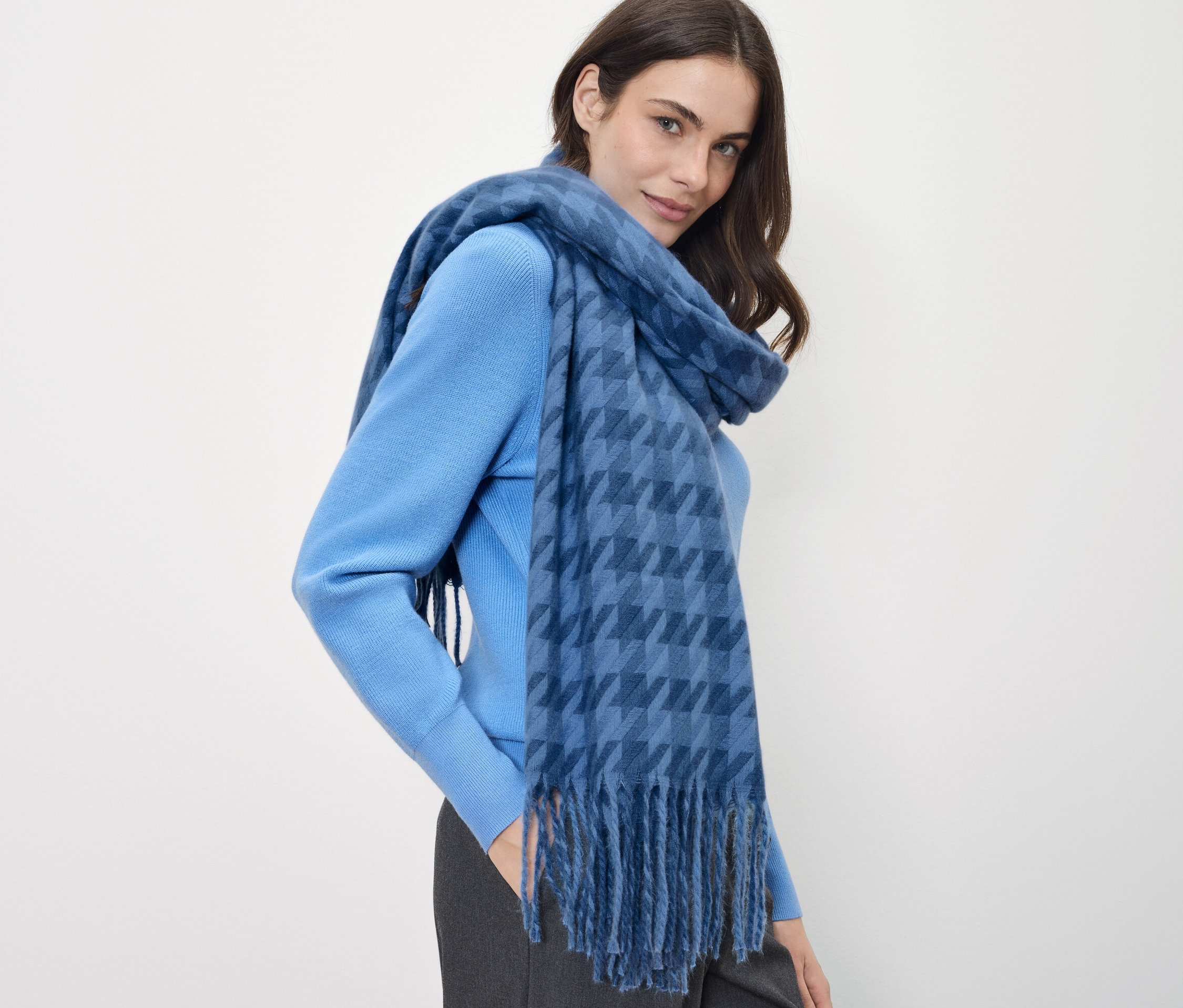 Kobieta z brązowymi włosami ma na sobie niebieski sweter i niebieski szal w kratę.