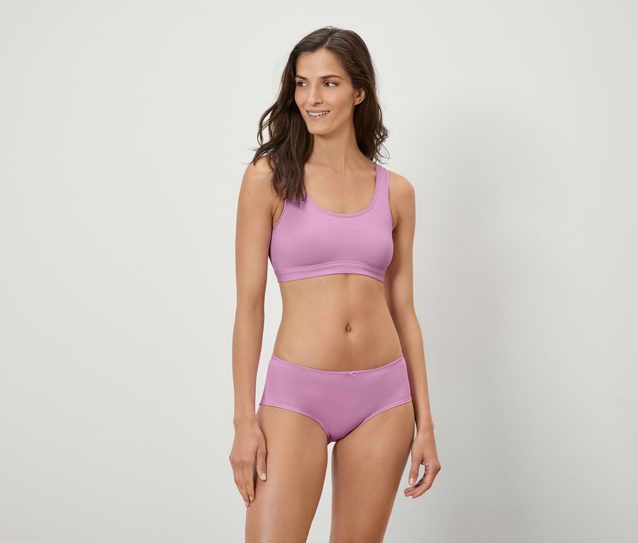 Kobieta pozuje w liliowym staniku sportowym i bokserkach.
