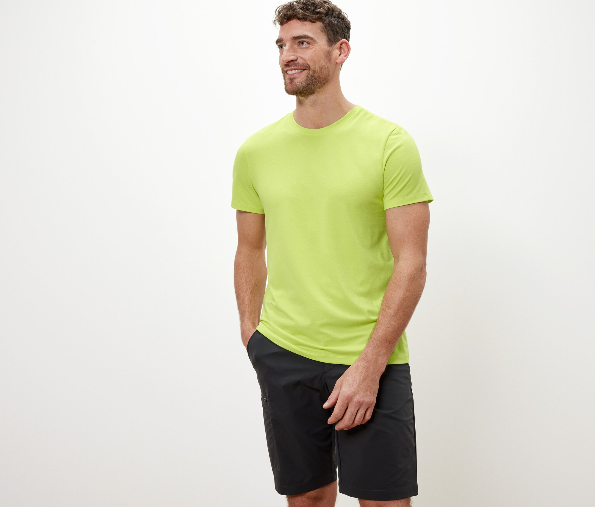 Mężczyzna o brązowych włosach pozuje na białym tle w limonkowej koszulce funkcyjnej.