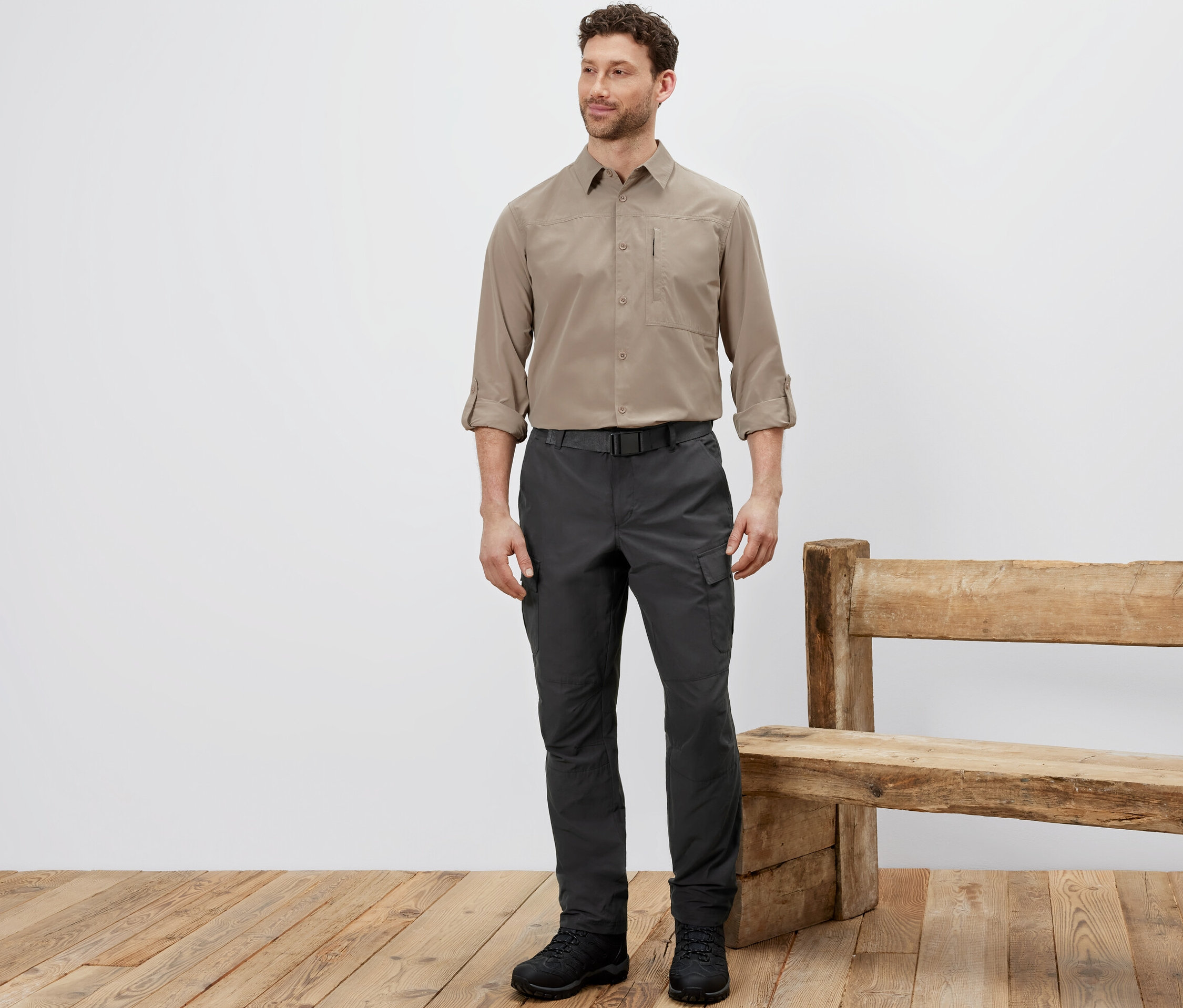 Mężczyzna stoi w spodniach outdoorowych z ochroną przed komarami, beżowej koszuli i czarnych butach.