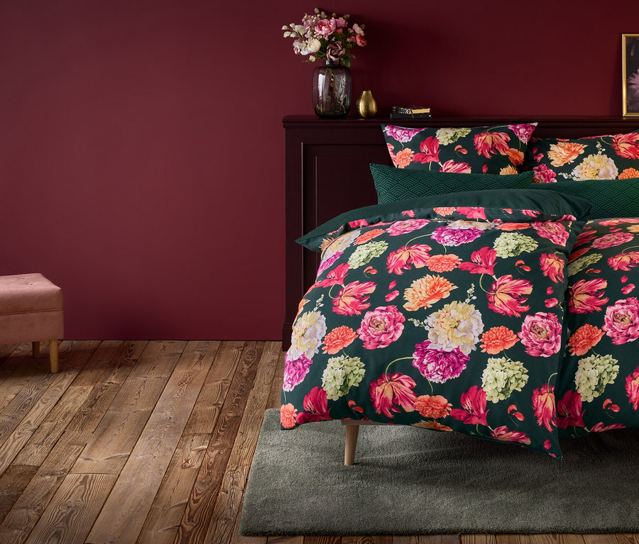 Kwiatowa pościel na łóżku ze stolikiem nocnym, lampą i różową ławką.