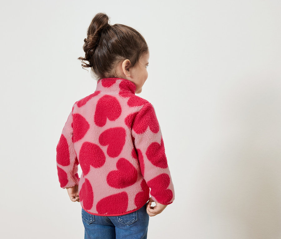 Mała dziewczynka w bluzie z czerwonymi sercami, patrzy w prawo.