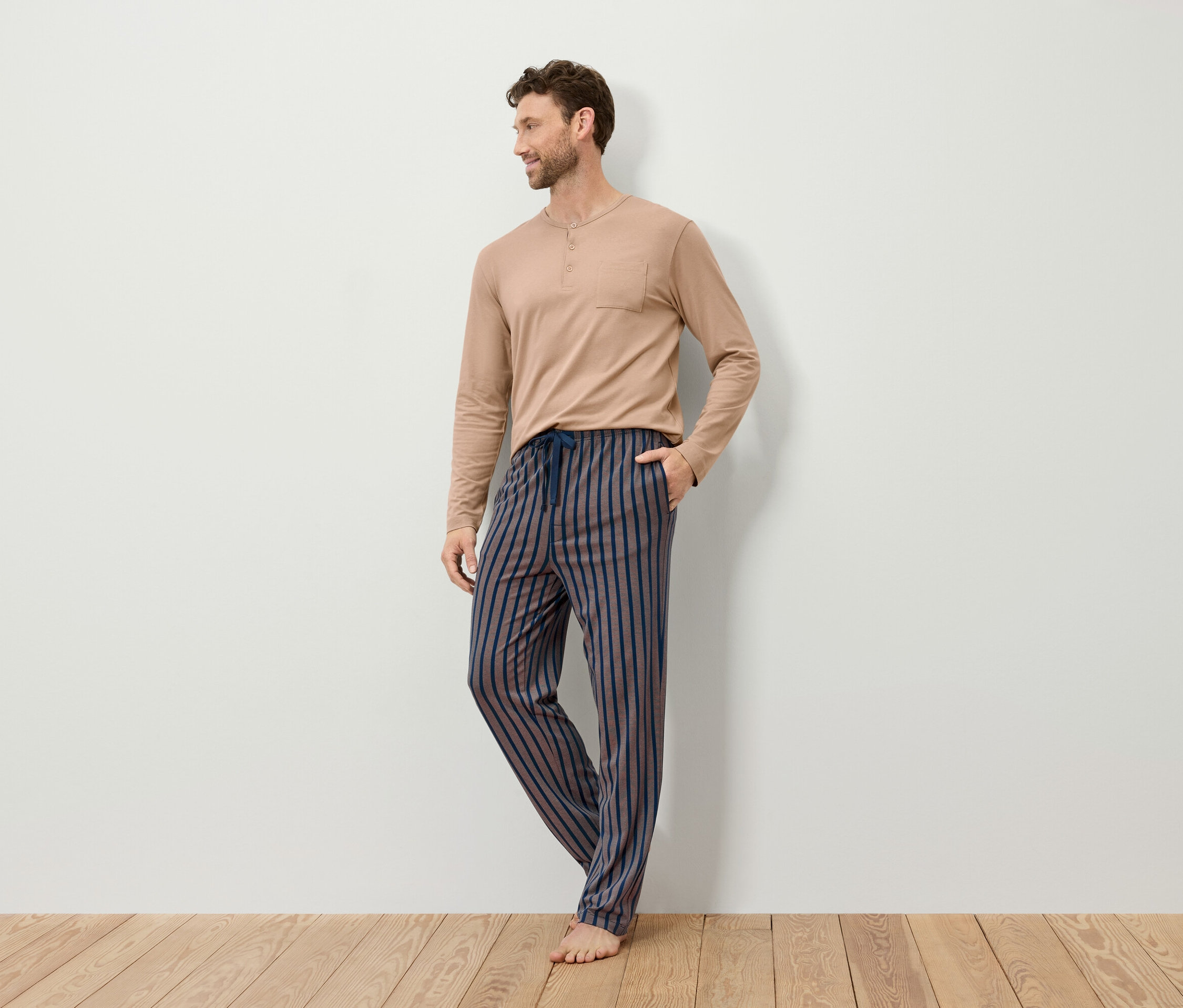 Mężczyzna w beżowej piżamie z długim rękawem i w paski spodniach od piżamy.