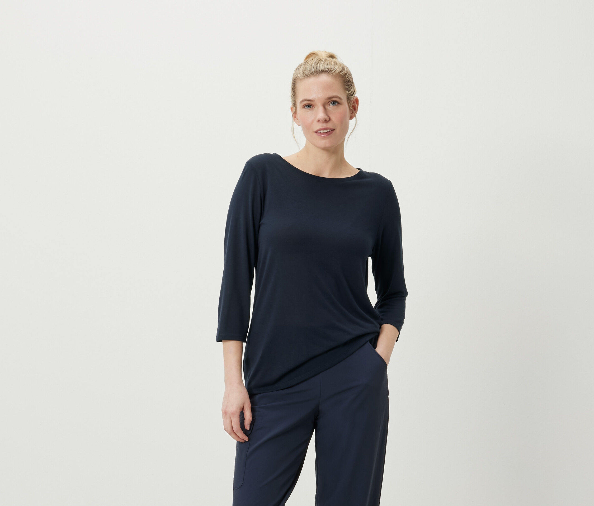 Kobieta pozuje w granatowej koszulce z rękawami trzy czwarte i spodniach.