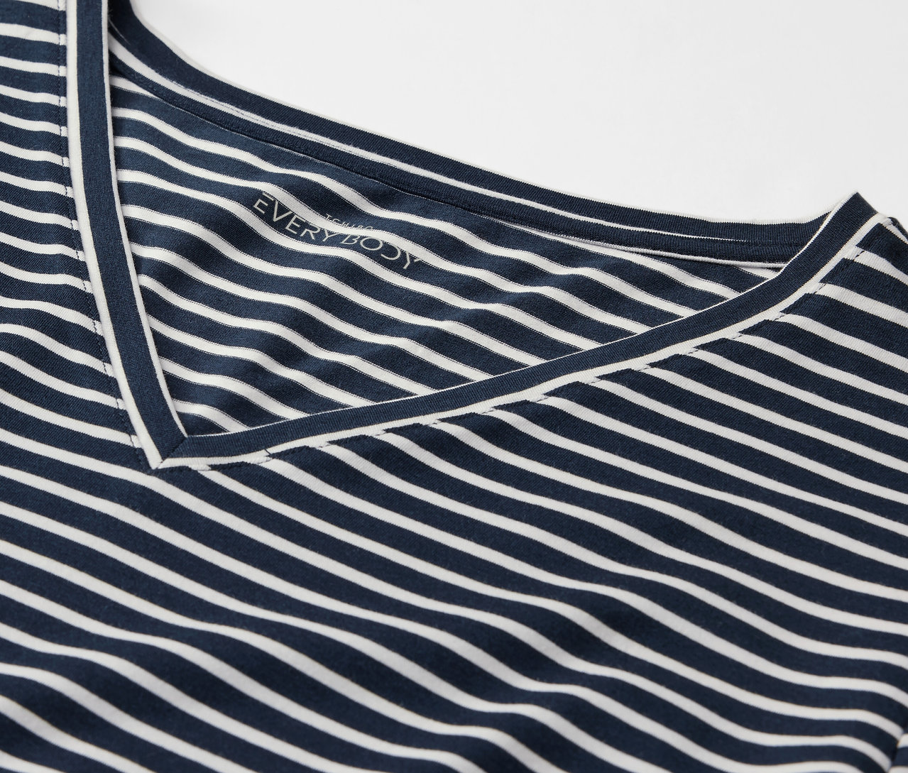 Szczegół granatowo-białej koszulki w paski z dekoltem w serek.