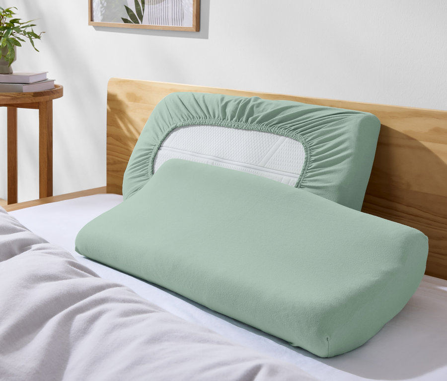 Dwie zielone poduszki na łóżku z białą pościelą.