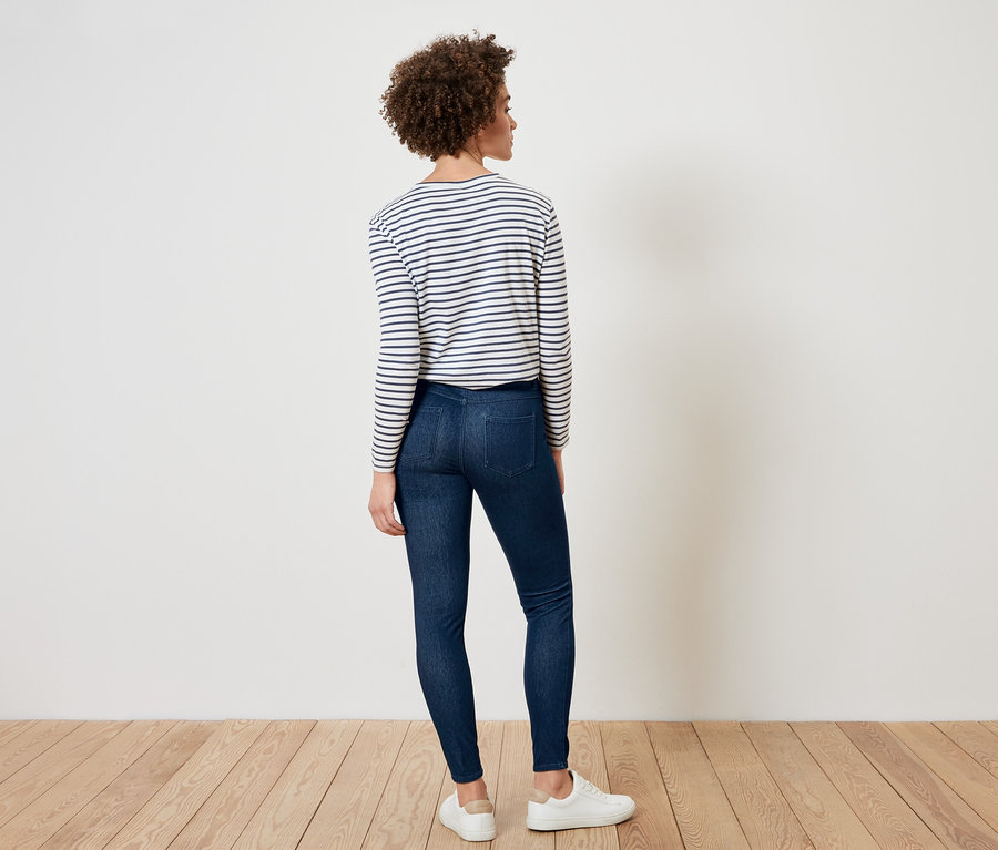 Kobieta stoi tyłem, ma na sobie bluzkę w paski, ciemne dżinsy i białe tenisówki.