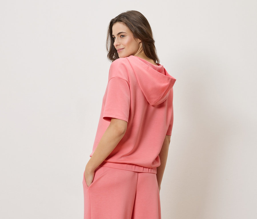 Kobieta ma na sobie koralową bluzę z krótkim rękawem i pasujące koralowe szorty.