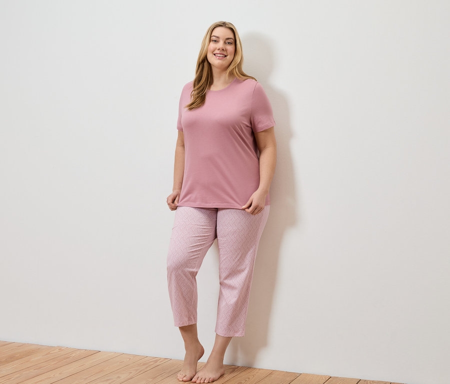 Uśmiechnięta blondwłosa kobieta w różowym T-shircie i różowych spodniach w geometryczny wzór.