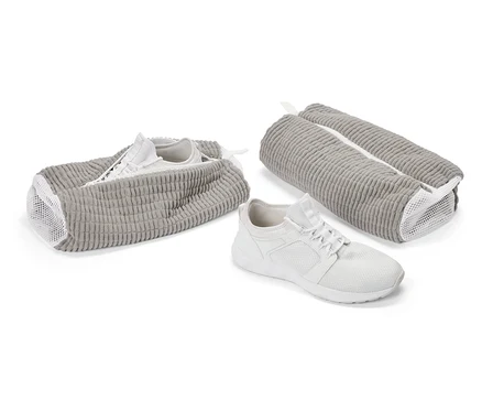 Biały but sportowy przed szarą torbą na buty. Kolejny but w otwartej torbie, trzecia torba jest zamknięta.