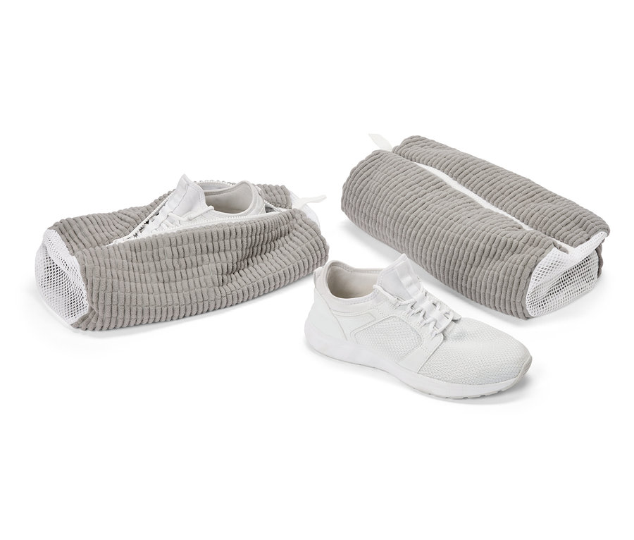 Biały but sportowy przed szarą torbą na buty. Kolejny but w otwartej torbie, trzecia torba jest zamknięta.