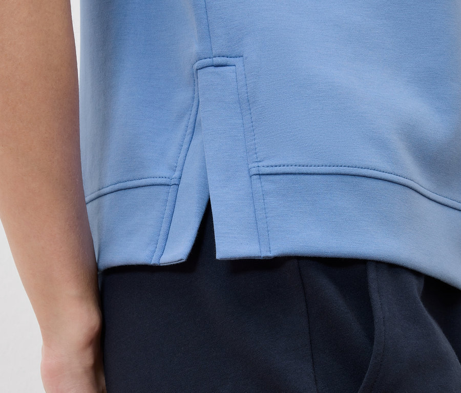 Zbliżenie na jasnoniebieską bluzę dresową z rozcięciem bocznym, założoną na granatowe spodnie.