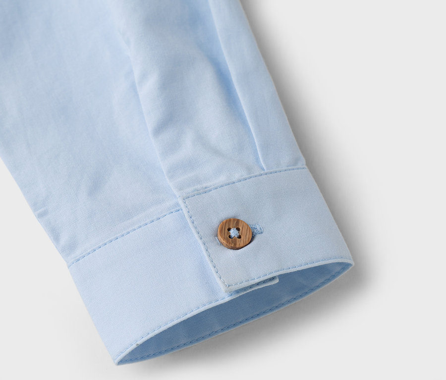 Zbliżenie rękawa jasnoniebieskiej koszuli z brązowym guzikiem.