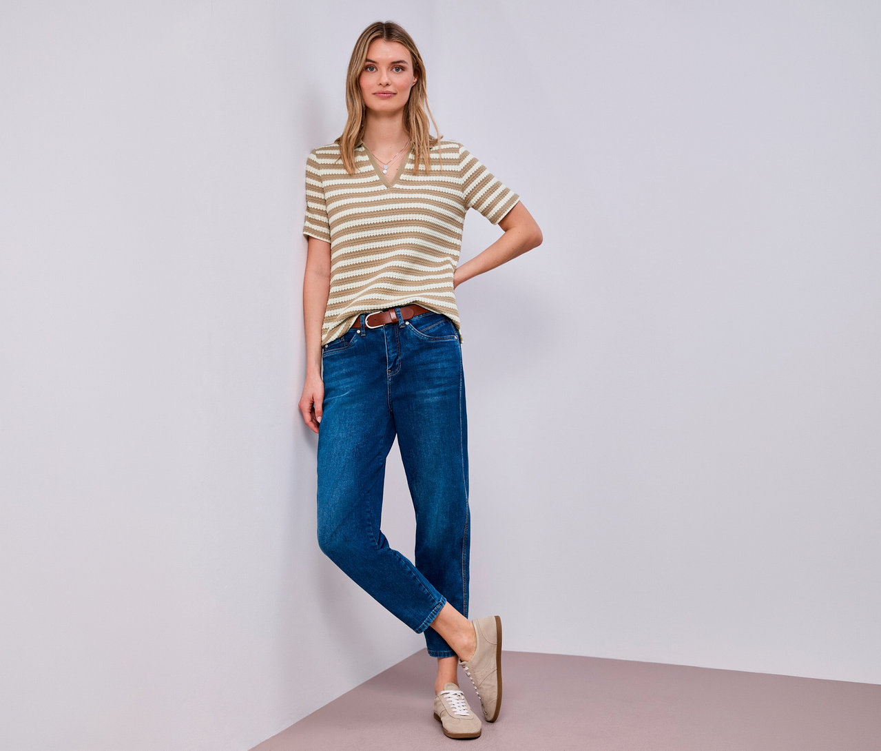 Kobieta pozuje w koszulce z dzianiny Street One, dżinsach, brązowym pasku i beżowych butach przy rogu.