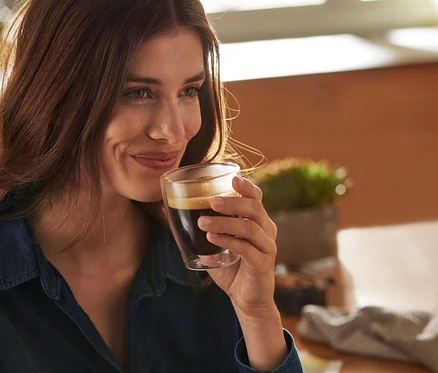 Uśmiechnięta kobieta trzyma szklankę o podwójnych ściankach do caffè crema.