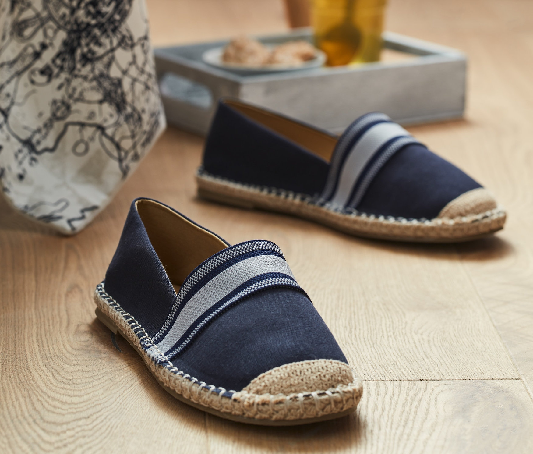 Dwa espadryle na drewnianej podłodze w pobliżu szklanki z napojem.