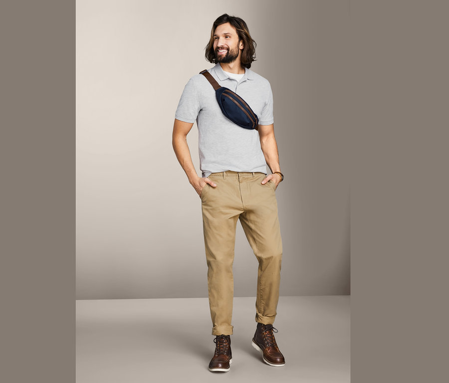 Mężczyzna z długimi włosami w szarej koszulce polo i khaki spodniach. Na piersi nosi saszetkę biodrową.