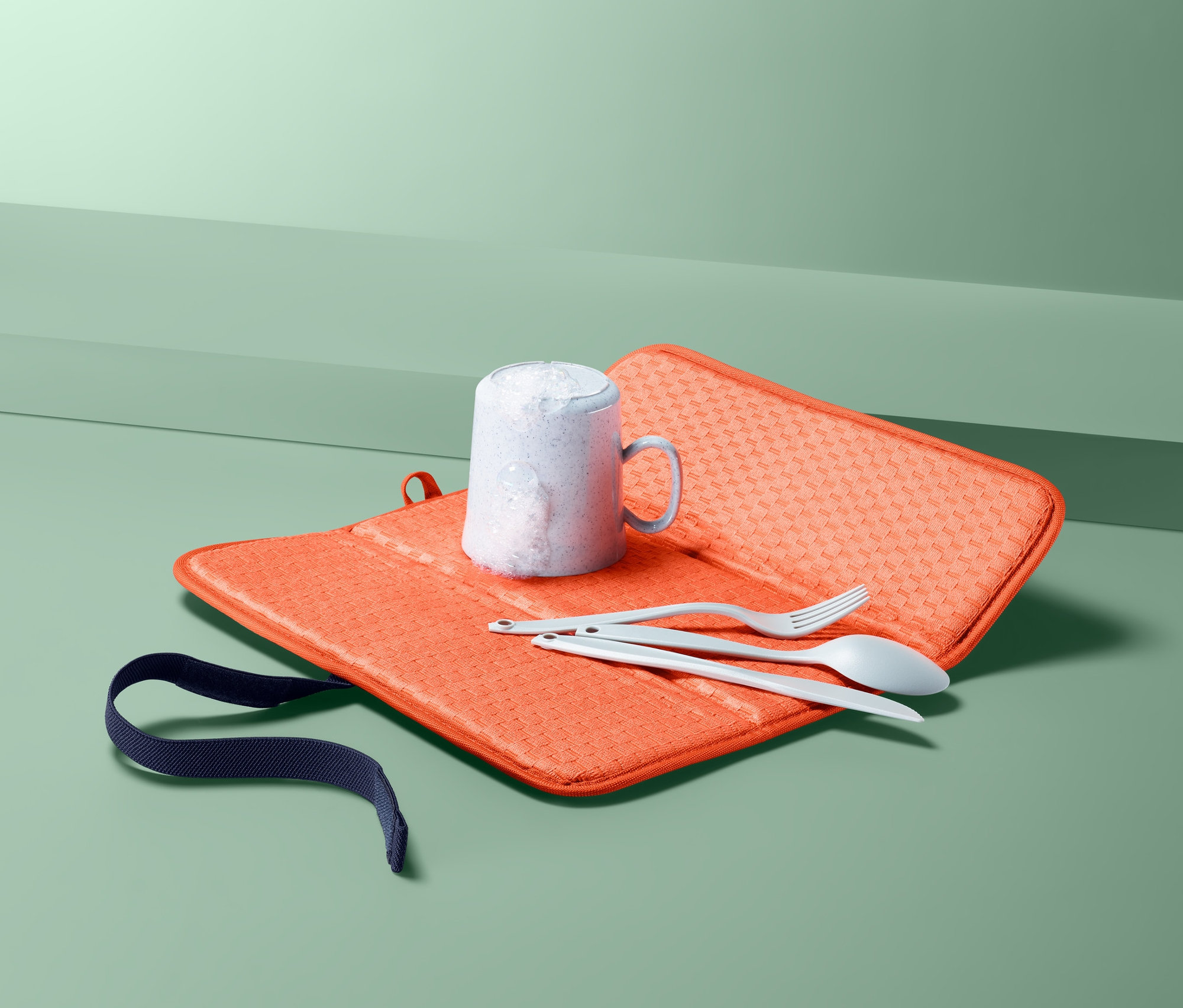 Kubek, nóż, widelec i łyżka na pomarańczowej składanej macie-ociekaczu.