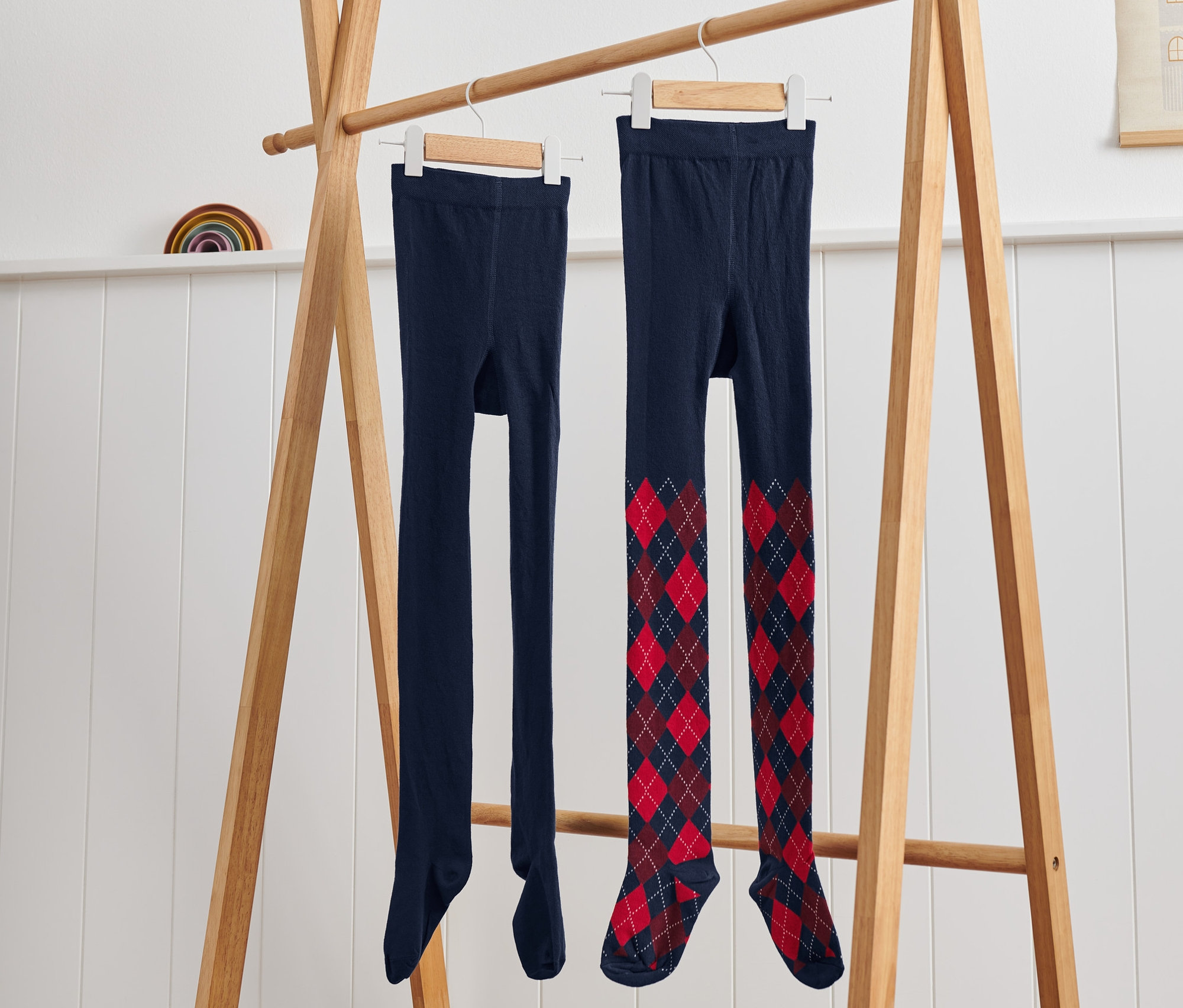 Na drewnianym stojaku wiszą rajstopy dziecięce w romby, 2 pary.