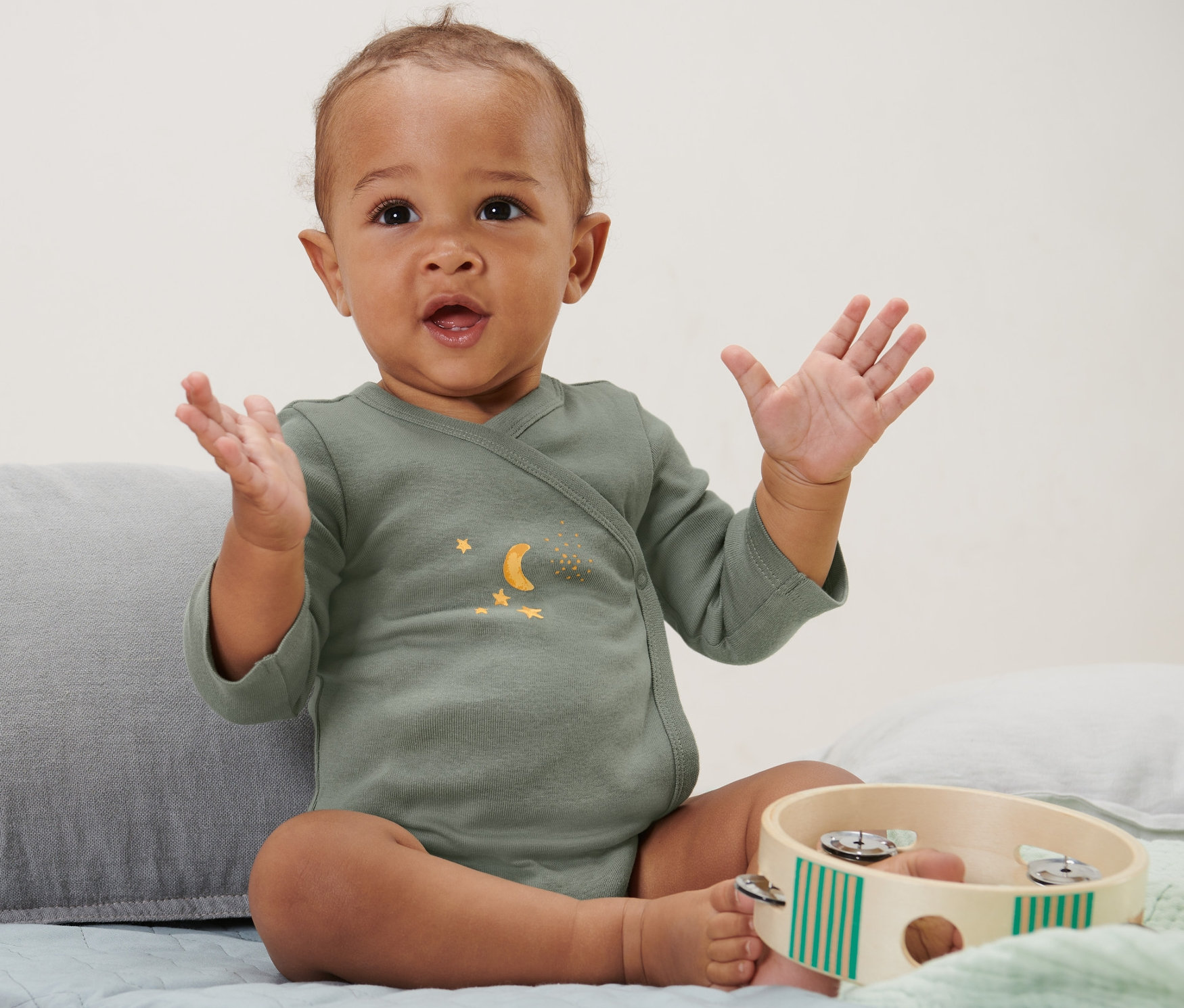 Siedzące dziecko macha rękami i ma na sobie body niemowlęce rosnące z dzieckiem, 5 par, gwiazdy.