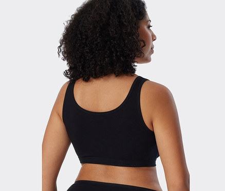 Widok z tyłu na kobietę z ciemnymi włosami, ubraną w czarne braletki z bawełną ekologiczną SCHIESSER, 2 sztuki.