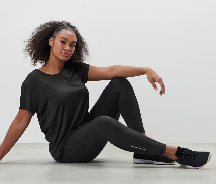 Kobieta siedzi na podłodze w czarnych legginsach sportowych i czarnej koszulce funkcyjnej.