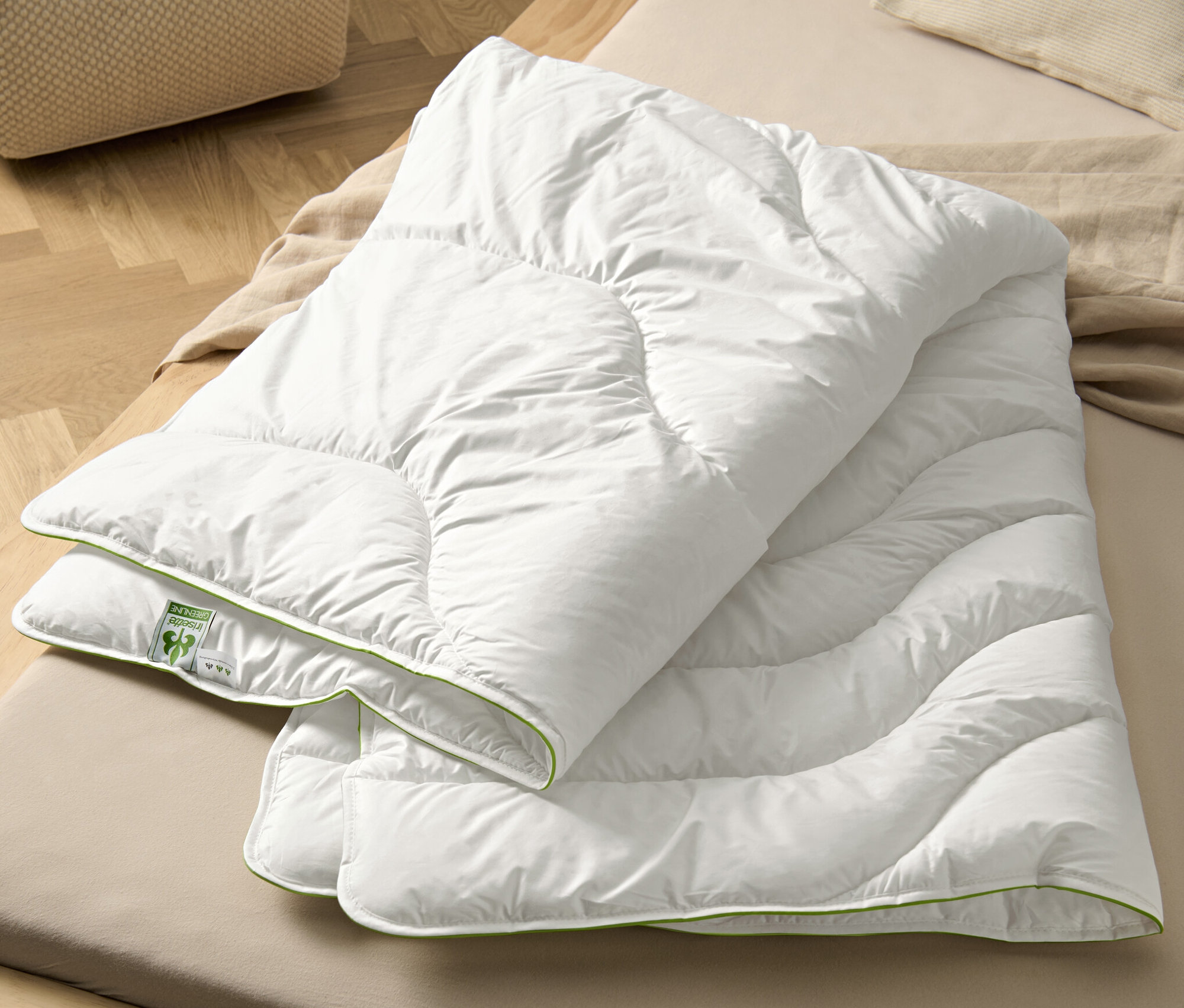 Na łóżku leży biała kołdra pikowana irisette® greenline Megafil® BIO.