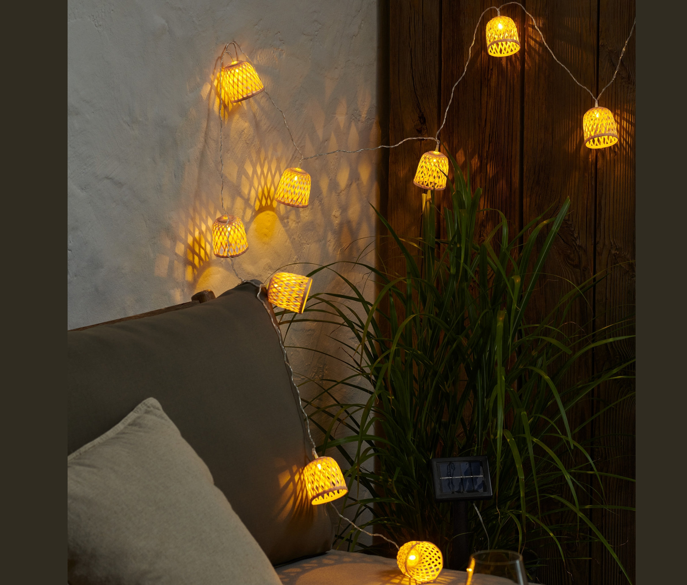 Świecący solarny łańcuch świetlny z dekoracyjnymi kloszami zwisa nad szarą sofą.