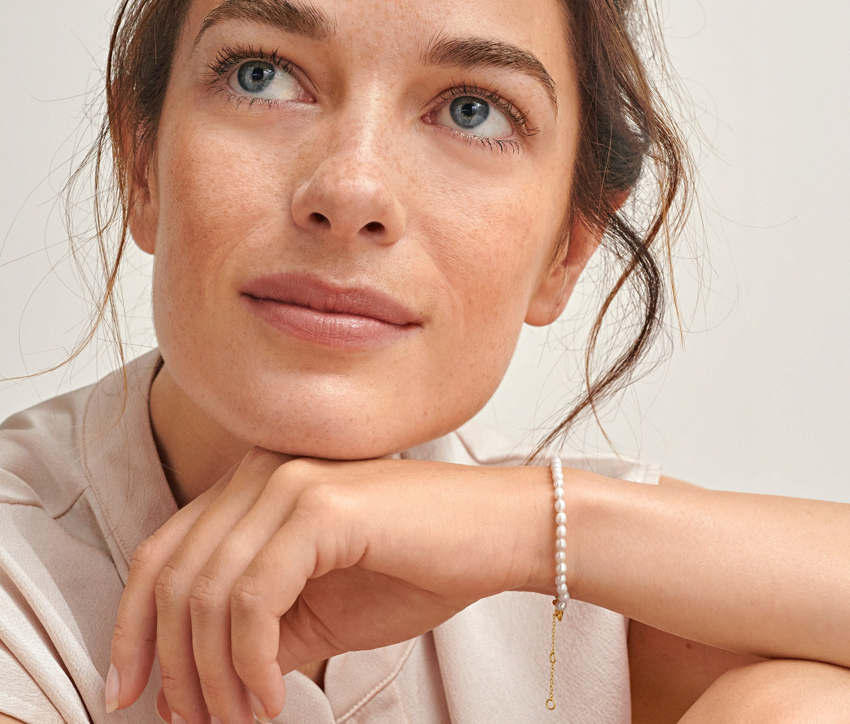 Kobieta patrzy w górę i nosi bransoletkę z pozłacanego srebra próby 925 ze słodkowodnymi perłami hodowlanymi.