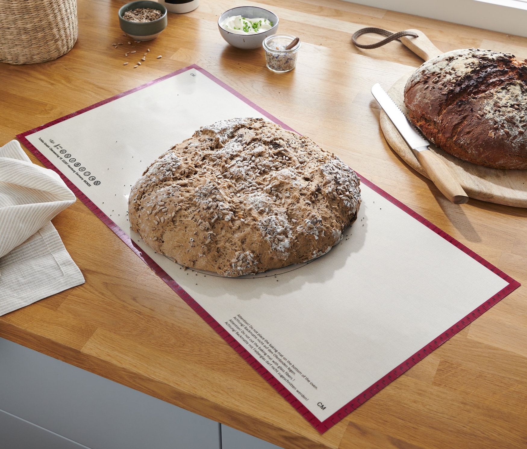 Bochenek chleba leży na Profesjonalnej macie do pieczenia XL na drewnianym blacie.